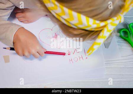 A small child draws congratulations on Mother's Day. A child with a postcard for mom. Holiday gift for mother Congratulations. Stock Photo