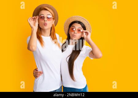 Happy stylish mother and daughter posing at studio yellow background, wearing straw hat and sunglasses. Summer family. Studio portrait of child with Stock Photo