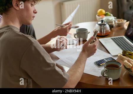 Cropped shot of serious thinking man paying utility bills payment online from home sitting in the kitchen with a laptop and paper invoices calculating Stock Photo