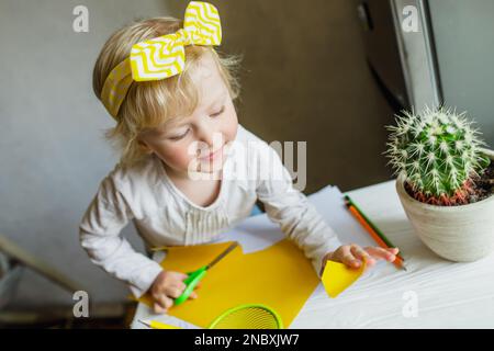 kid cutting paper for greeting card on mothers day. child makes applications from colored paper. Stock Photo
