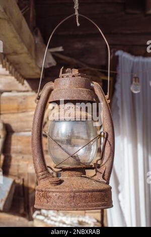 Old rusty lantern hanging on the doorstep roof of a wooden house, vertical Stock Photo
