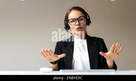 Businesswoman in glasses and headset participating in corporate web conference leading business online meeting. Stock Photo