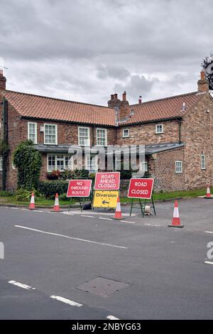 A cluster of roadworks signs - road closed, diversion, no through route - and traffic cones block a suburban street while repairs are carried out. Stock Photo