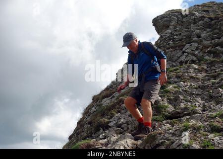 Old Man Walking Down Steep Rocky Crag from Parkhouse Hill in the Dove Valley in the Peak District National Park, England, UK. Stock Photo