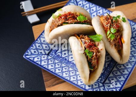 Food concept Homemade organic Pulled Beef Bao Buns or Gua Bao in sqare plate on black background with copy space Stock Photo