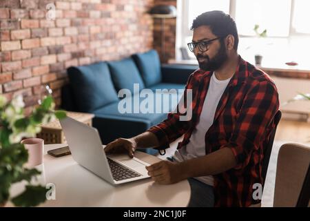 Happy indian man freelancer or entrepreneur have video conference talking, working remotely online at home office - video call and diversity Stock Photo