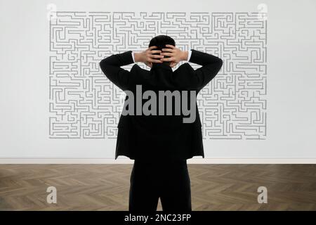 Businessman looking at wall with illustration of maze indoors Stock Photo