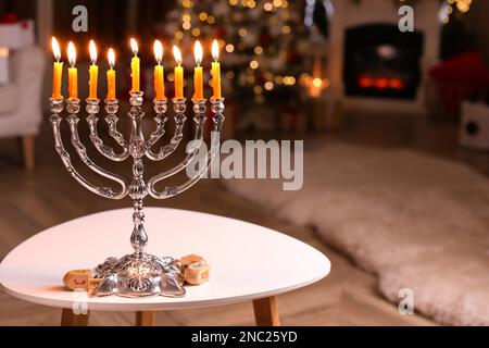 Silver menorah near dreidels with symbols He, Pe, Nun, Gimel on white table in room, space for text Stock Photo