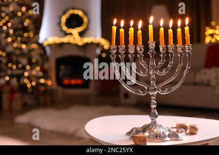 Silver menorah near dreidels with symbols He, Pe, Nun, Gimel on white table in room, space for text Stock Photo