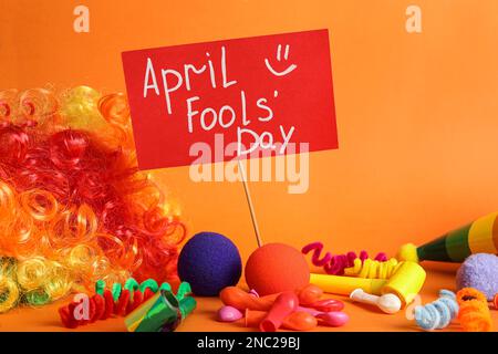 Sign with phrase Happy Fools' Day and clown's accessories on orange background Stock Photo