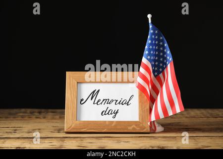 Frame with phrase Memorial Day and American flag on wooden table against black background Stock Photo