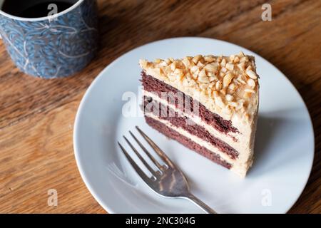 A slice of freshly baked, peanut butter and chocolate cake. The cake has a thick buttercream filling and is served on a side plate with a cup of tea Stock Photo