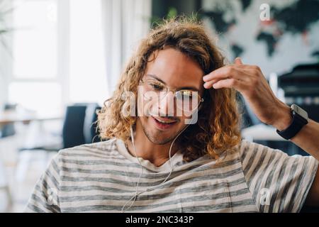 Young curly man in eyeglasses using earphones while working in office Stock Photo