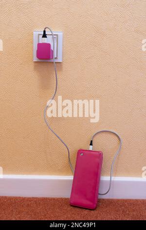 Mobile phone on a floor with a pink case plugged in & charging with a pink USB plug & a cable. Concept: women and technology, feminine phone accessory Stock Photo