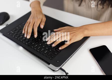 Young black woman typing text on laptop keyboard. POC female working on modern notebook pc in overhead photo Stock Photo