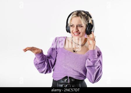 Cute caucasian woman wearing lilac ribbed blouse isolated over white background listens to music by touching headphones is having a lot of fun. Dj pla Stock Photo