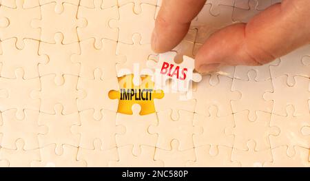 Implicit bias symbol. Concept words Implicit bias on white paper puzzles. Beautiful yellow table yellow background. Businessman hand. Business psychol Stock Photo