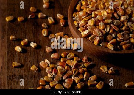 Corn grains in a wooden bowl and in bulk on a wooden table Stock Photo