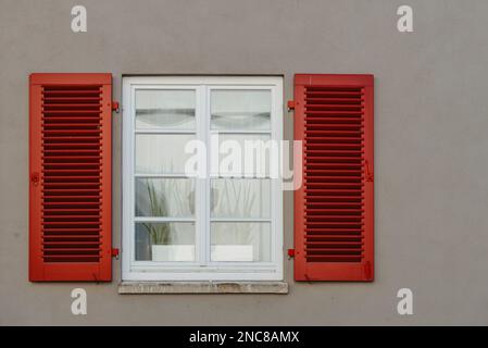 Italian windows on the white wall facade with open red color classic shutters and flowers on the windows. window shutter wall Stock Photo