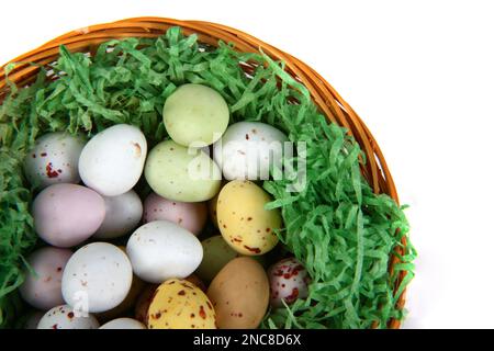 Chocolate mini Easter eggs in green straw on a whicker basket against a white background Stock Photo