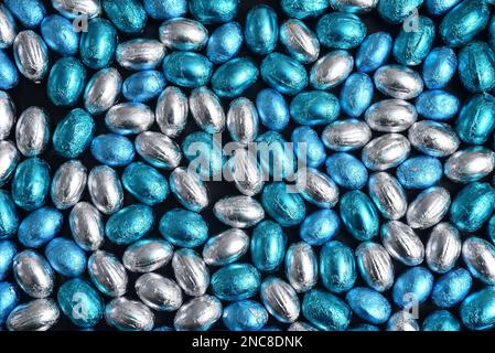 Blue,  silver and turquoise foil wrapped chocolate easter eggs, against a black background. Stock Photo