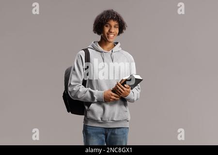 African american male student with a backpack holding books and smiling isolated on gray background Stock Photo