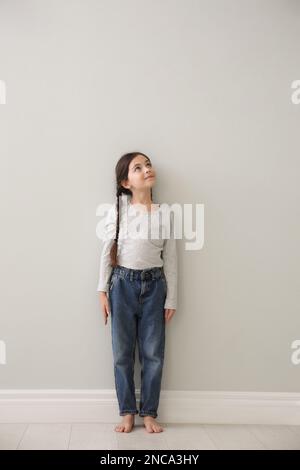 Little girl measuring her height near light grey wall indoors Stock Photo