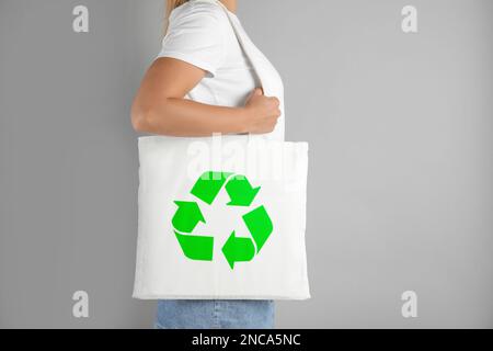 Woman holding bag with recycling symbol on grey background Stock Photo