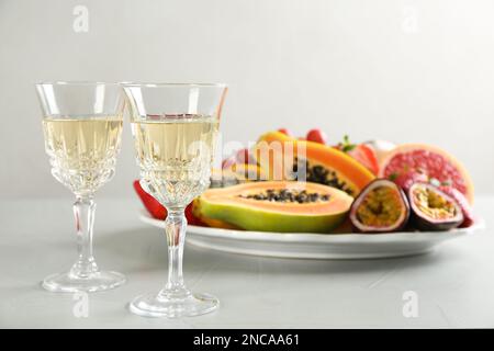 Delicious exotic fruits and glasses of wine on light grey table Stock Photo