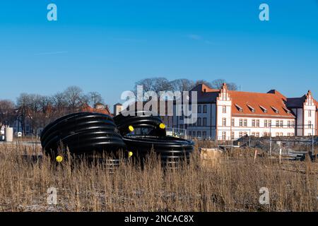 Large rolls of black plastic pipes with yellow plugs at a construction site against residential buildings. Stock Photo