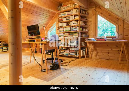 Wooden desk table with computer and bookcase in home office set-up on mezzanine inside piece sur piece Scots pine log home. Stock Photo
