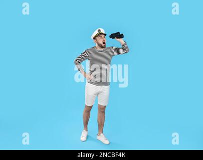 Shocked sailor with binoculars on light blue background Stock Photo