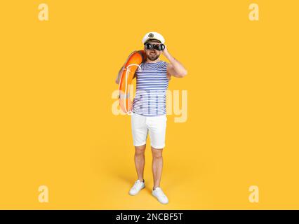 Sailor with binoculars and ring buoy on yellow background Stock Photo
