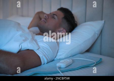 Man sleeping on electric heating pad in bed at night Stock Photo