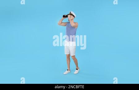Sailor looking through binoculars on light blue background Stock Photo