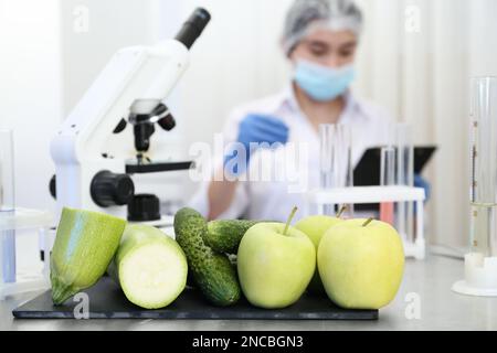 Fresh vegetables, fruits on table and scientist proceeding quality control in laboratory Stock Photo