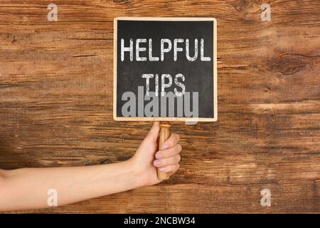 Woman holding small chalkboard with text Helpful Tips on wooden background, closeup Stock Photo
