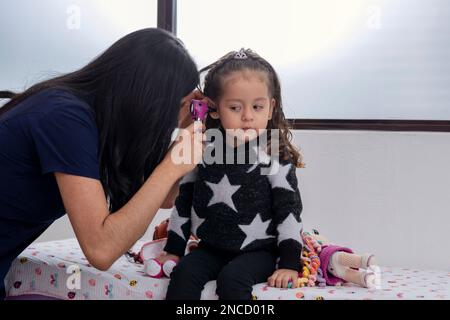 Young Latina doctor checks a young girl's ear with an otoscope in her medical office. Stock Photo