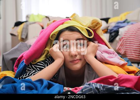 Pensive young woman with lots of clothes on floor in room. Fast fashion Stock Photo