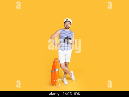 Sailor with binoculars and ring buoy on yellow background Stock Photo