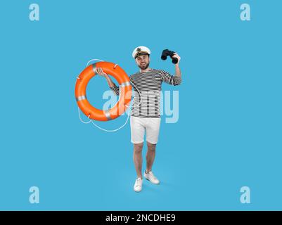 Sailor with binoculars and ring buoy on light blue background Stock Photo