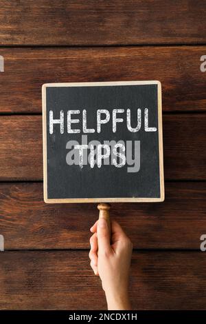 Woman holding chalkboard with phrase Helpful Tips on wooden background, closeup Stock Photo