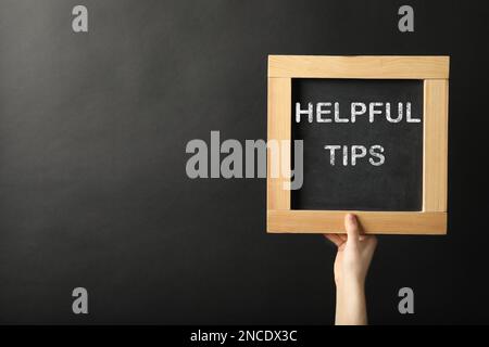 Woman holding chalkboard with phrase Helpful Tips on black background, closeup. Space for text Stock Photo