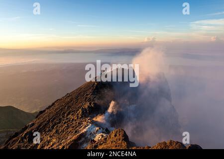 Merapi volcano crater rim with people climbing up the summit at sunrise ...