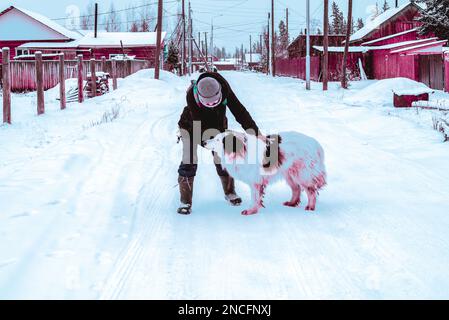 Abstract cyberpunk style photo of a girl playing with a white dog in the snow on a village road in Yakutia. Stock Photo