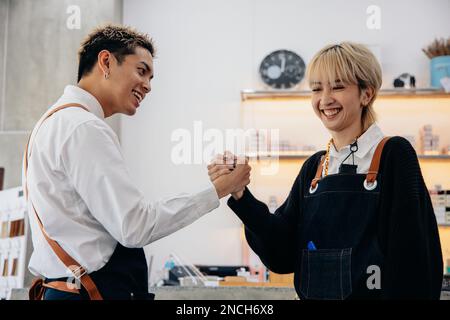 Cheerful young Asian man and woman hairdresser wearing apron uniform in modern salon giving high-five to each other on celebrating success of salon Stock Photo