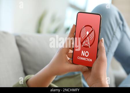 Woman holding mobile phone with text NO CONNECTION on screen at home Stock Photo