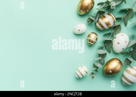 Easter eggs painted in gold and eucalyptus branches on a soft green background. Festive background Stock Photo