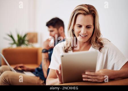 I love doing what I do. an attractive young businesswoman sitting and using a tablet while her colleagues work behind her. Stock Photo