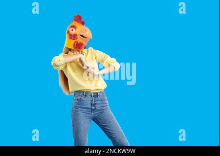 Young woman wearing funny strange chicken mask dancing on blue studio background Stock Photo